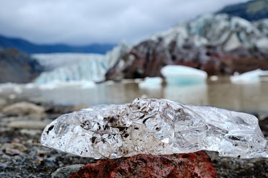 A detailed view of a transparent ice chunk with a blurred glacier backdrop.
