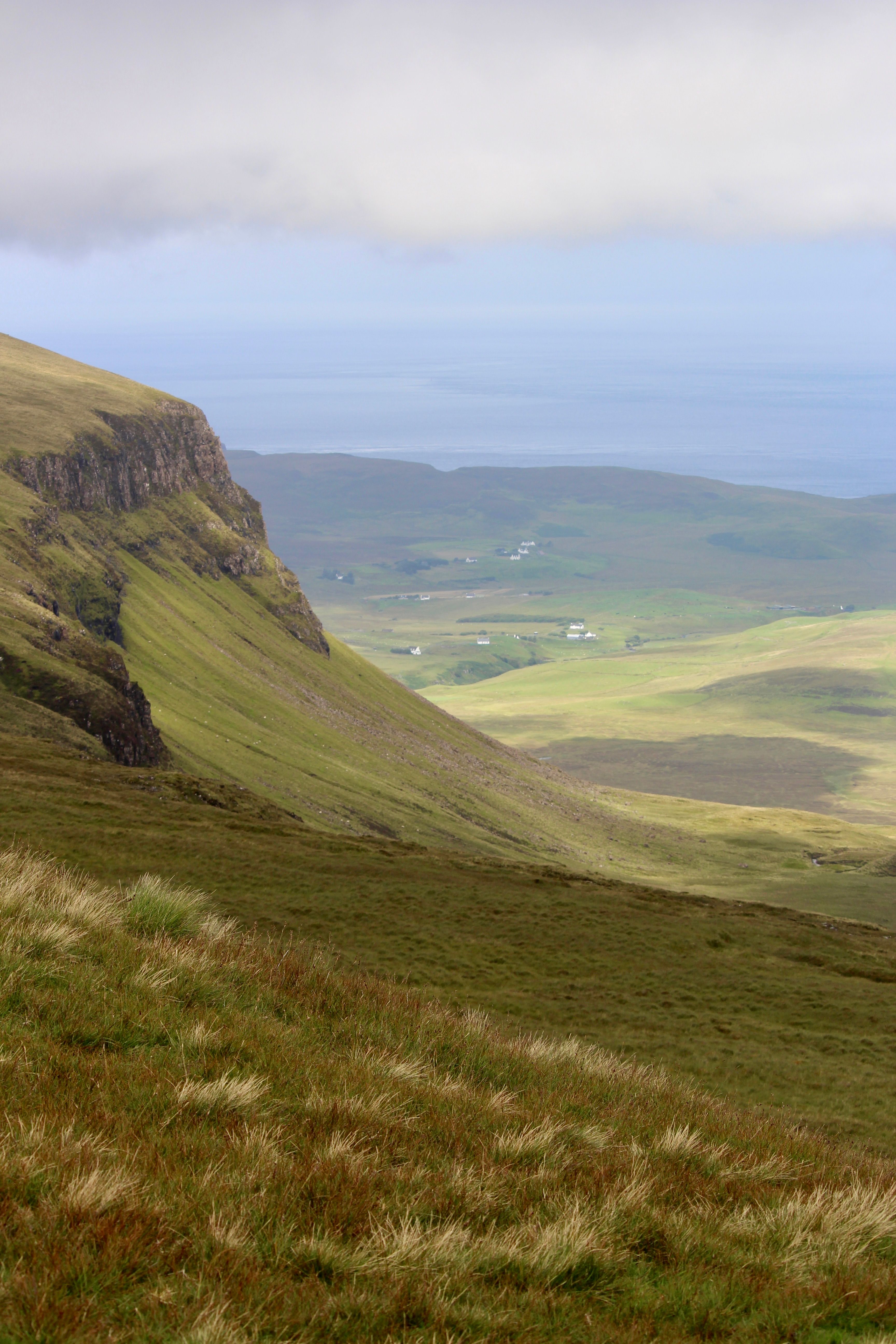 Scenic landscape of lush green hills overlooking a vast ocean under cloudy skies.