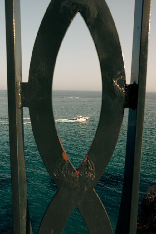 Free A small boat navigating the calm waters of the Mediterranean Sea, framed by an iron fence in Spain. Stock Photo