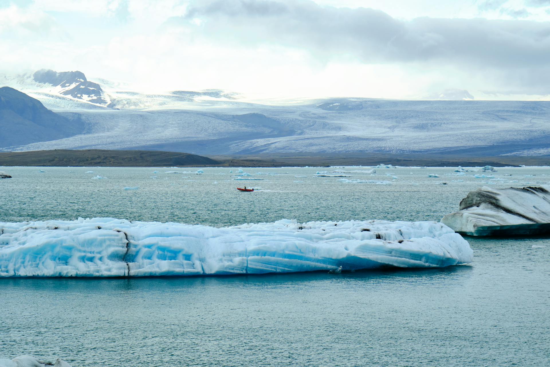 A stunning view of icebergs floating in a polar sea with mountains in the background and a kayak in the distance.