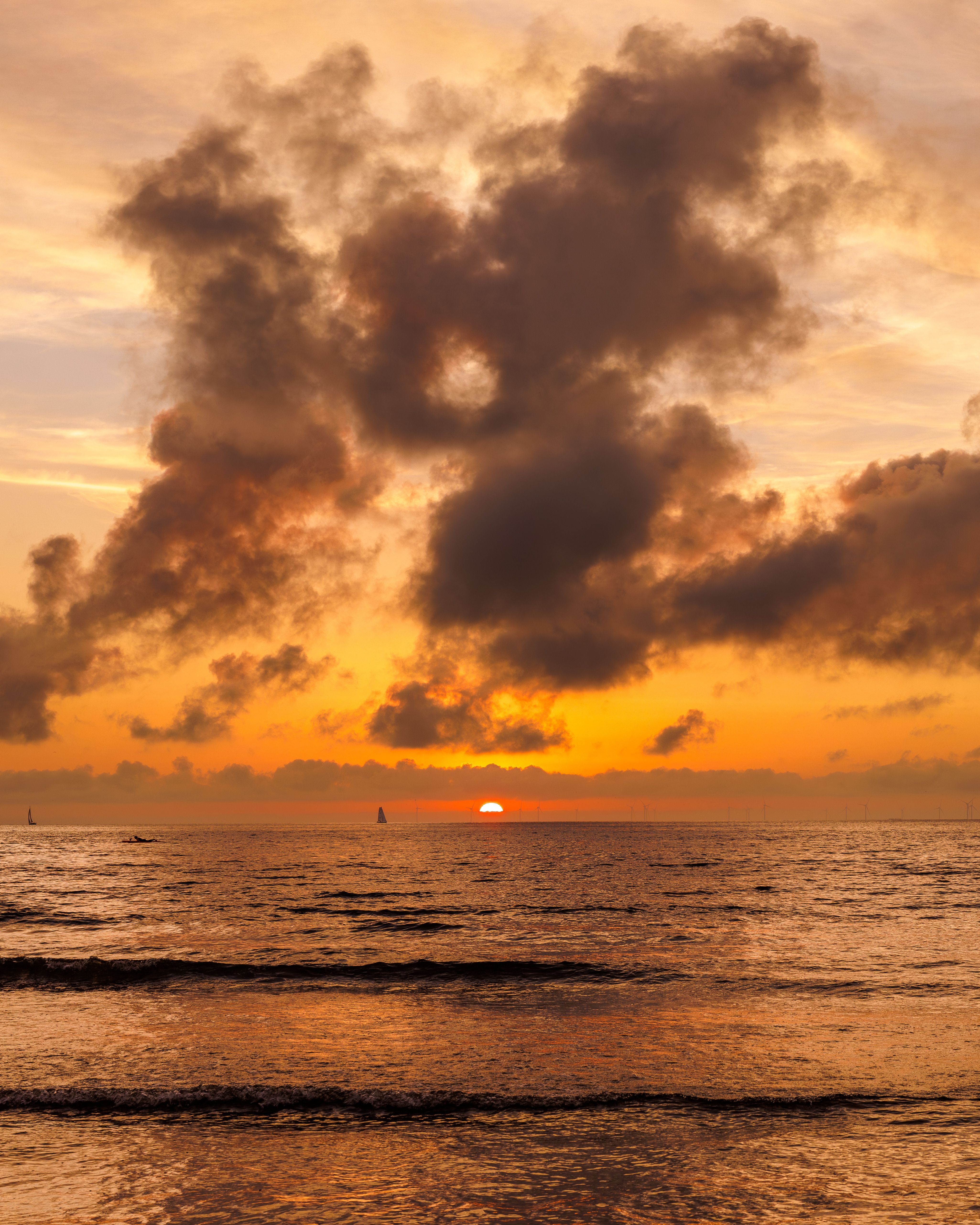 A sunset over the ocean with clouds and a boat · Free Stock Photo