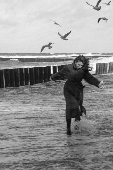 Black and white image of a woman running on the beach with seagulls in autumn.