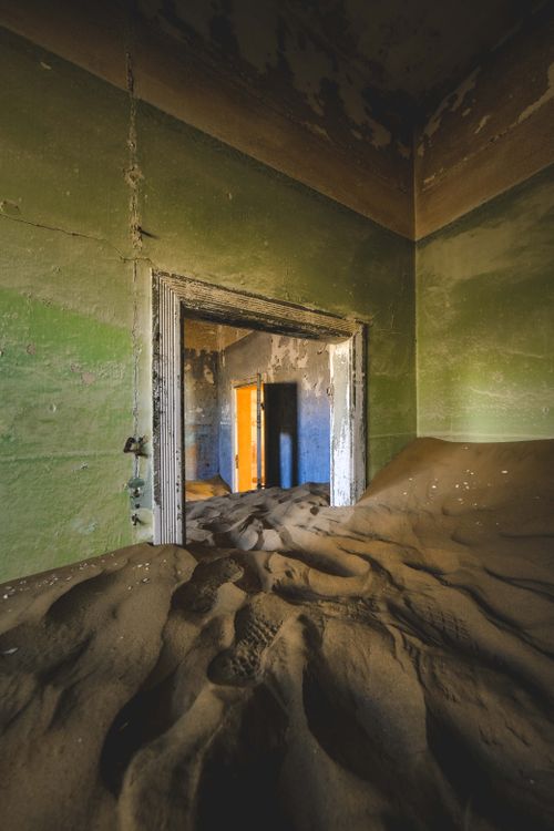 Free A deserted, sand-filled room in a house with weathered green walls, evoking decay and solitude. Stock Photo