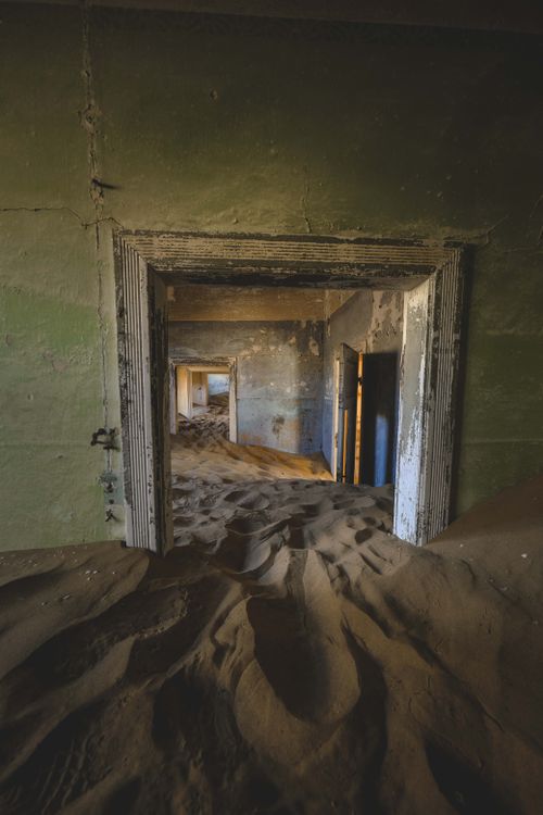 Free A haunting view of an abandoned building corridor filled with desert sand, showcasing decay and time's passage. Stock Photo