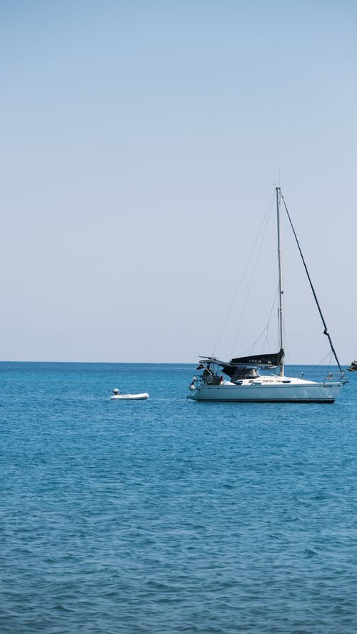 Free A serene sailboat drifting on a calm ocean under a blue sky, perfect for leisure travel. Stock Photo
