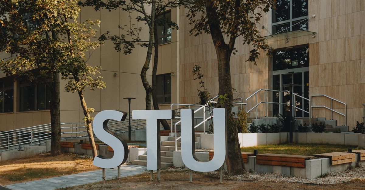 Modern building entrance with large STU letters surrounded by greenery and urban design.