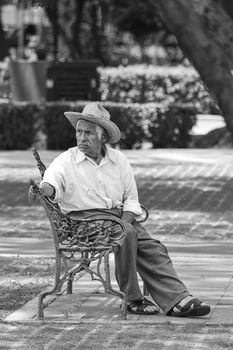 Black and white photo of elderly man in outdoor park setting, sitting and reflective.