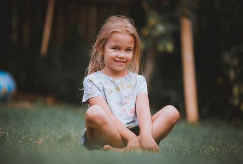 Free Young girl enjoys a sunny day sitting on grass, expressing joy and innocence. Stock Photo