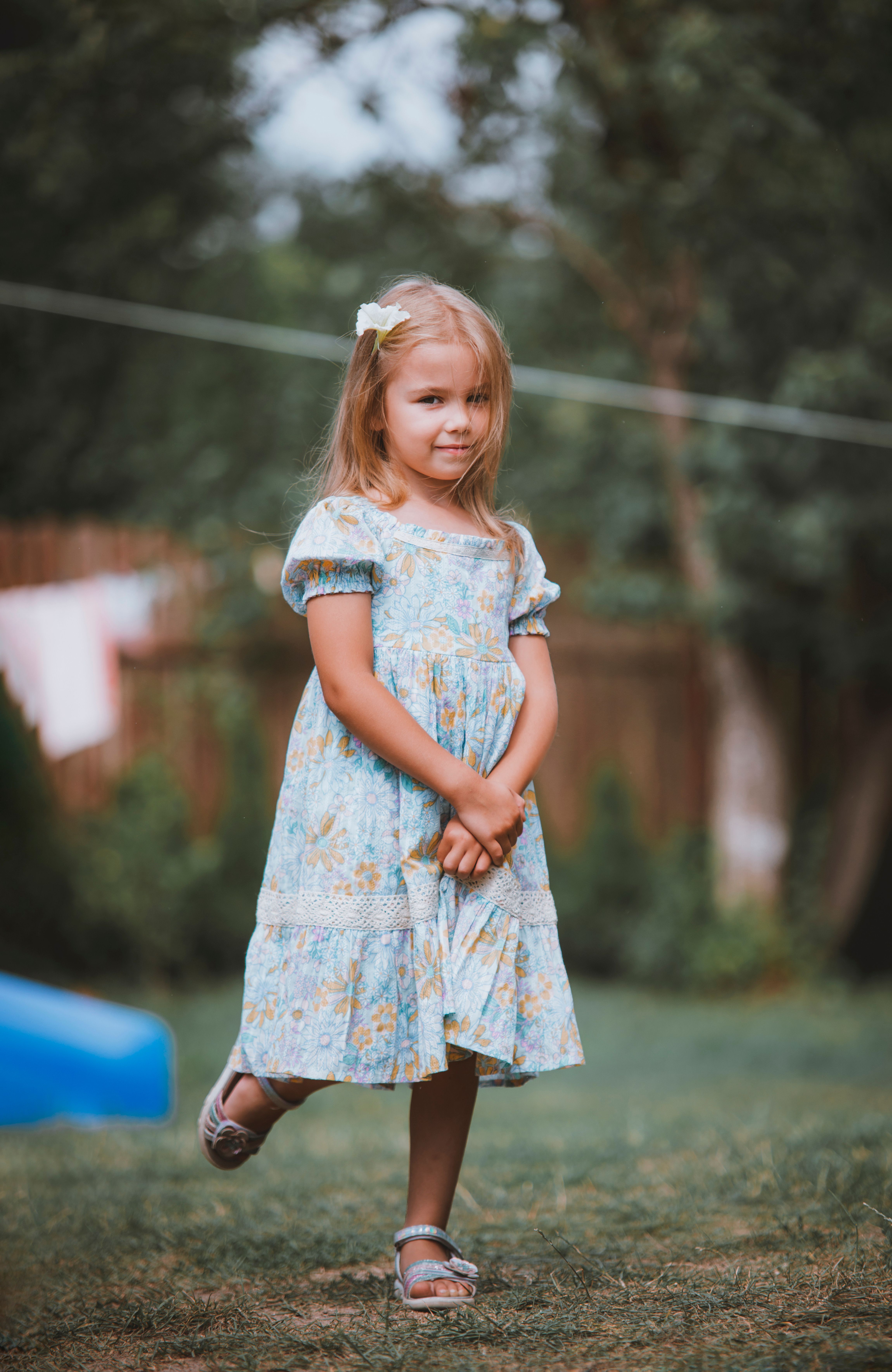 A little girl in a blue dress standing in the grass · Free Stock Photo