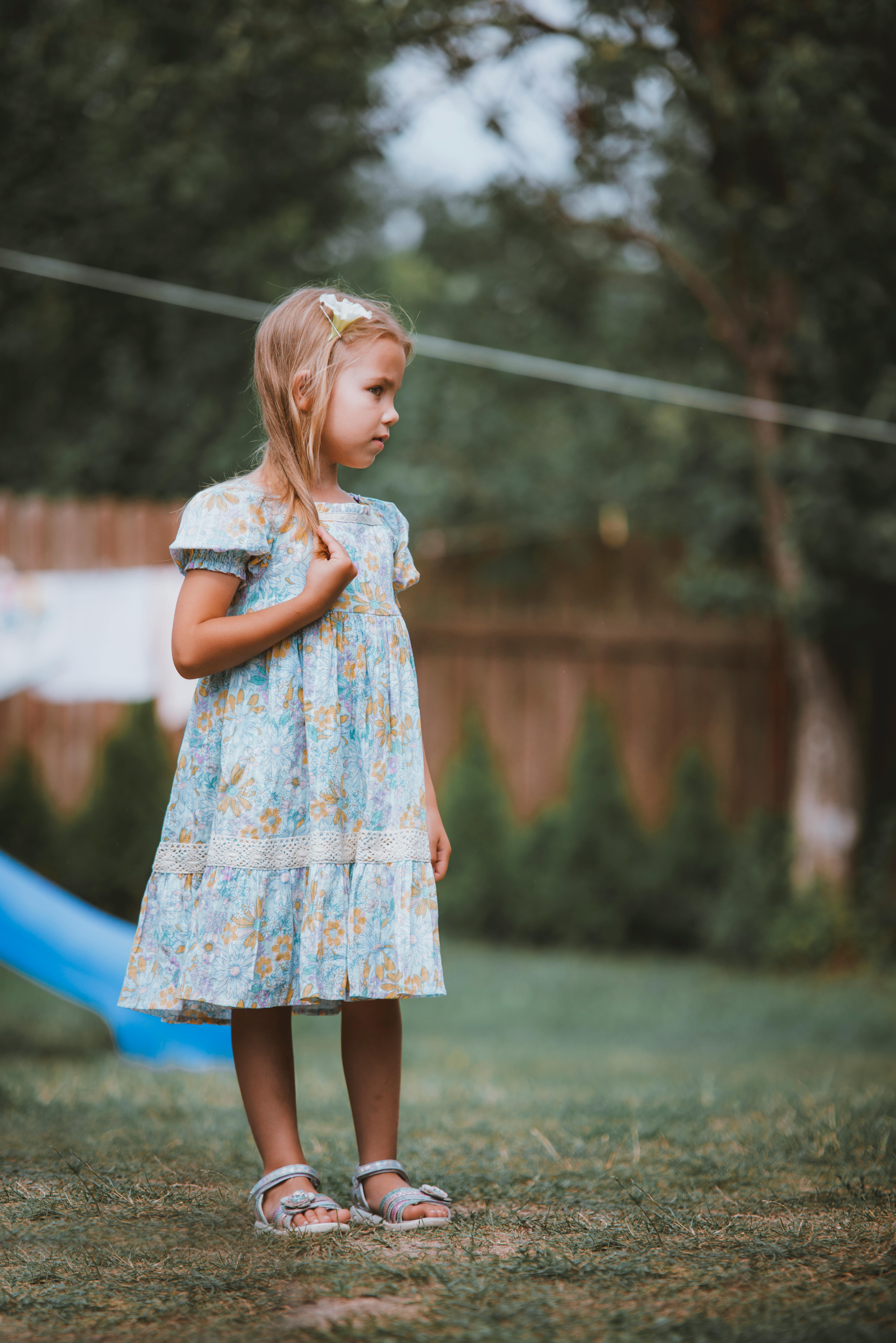 a little girl standing in the grass wearing a dress