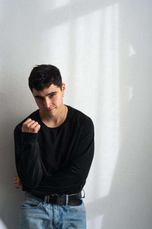 Free A young man stands indoors, casting a pensive and stylish look against a light-filled wall. Stock Photo