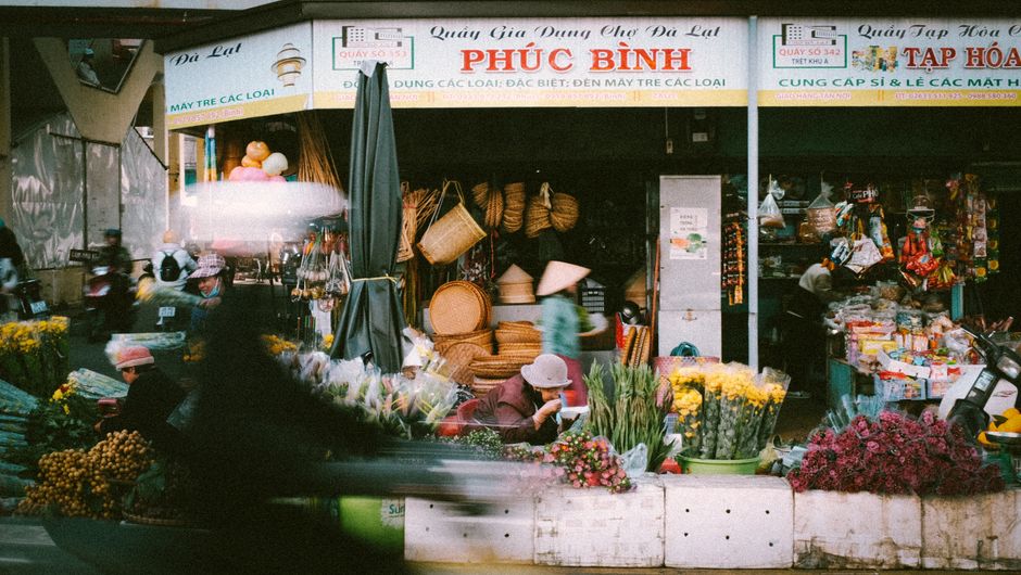 A bustling street market with colorful flowers and local vendors selling products in Da Lat.
