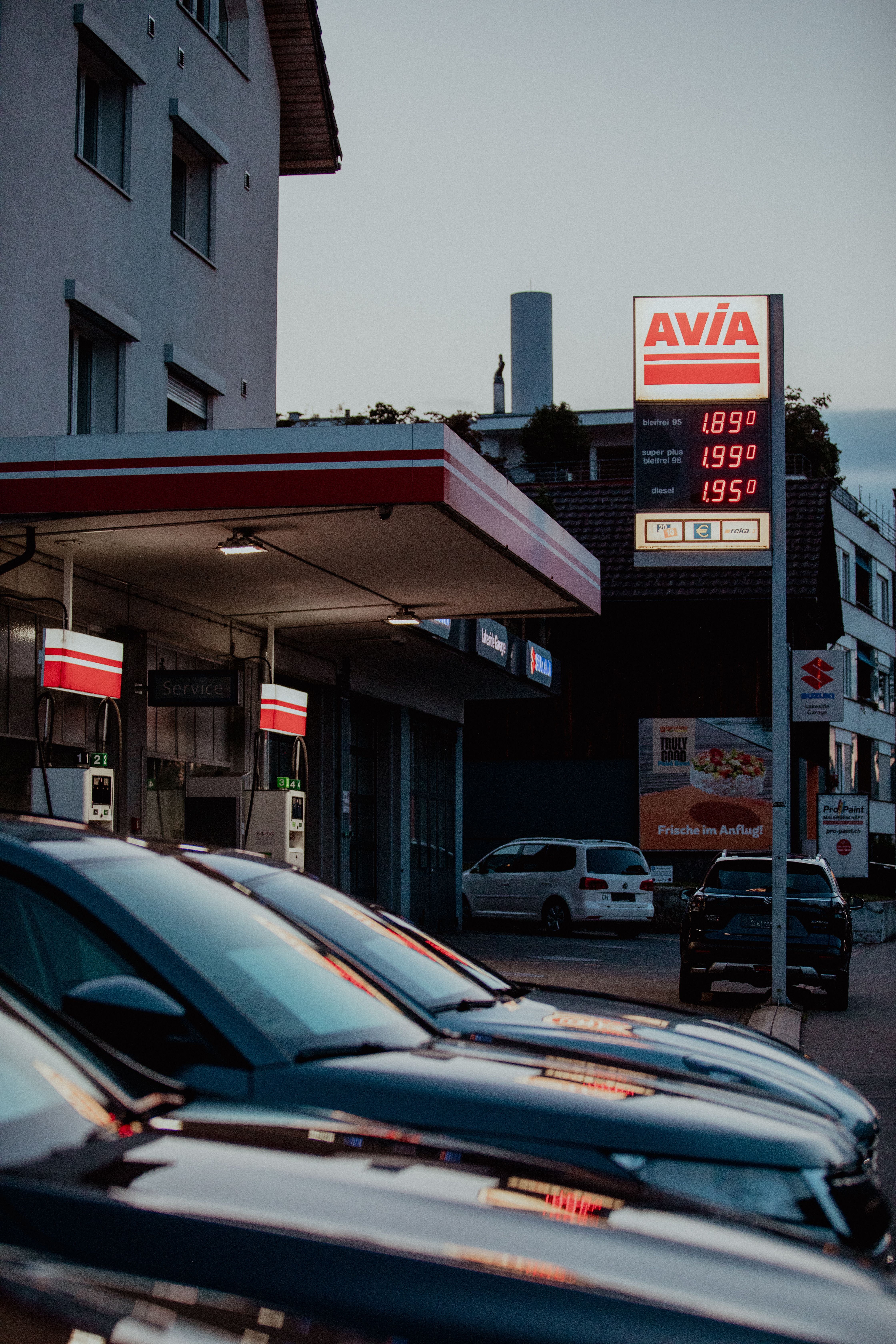A modern AVIA gas station with cars parked and prices displayed during evening twilight.