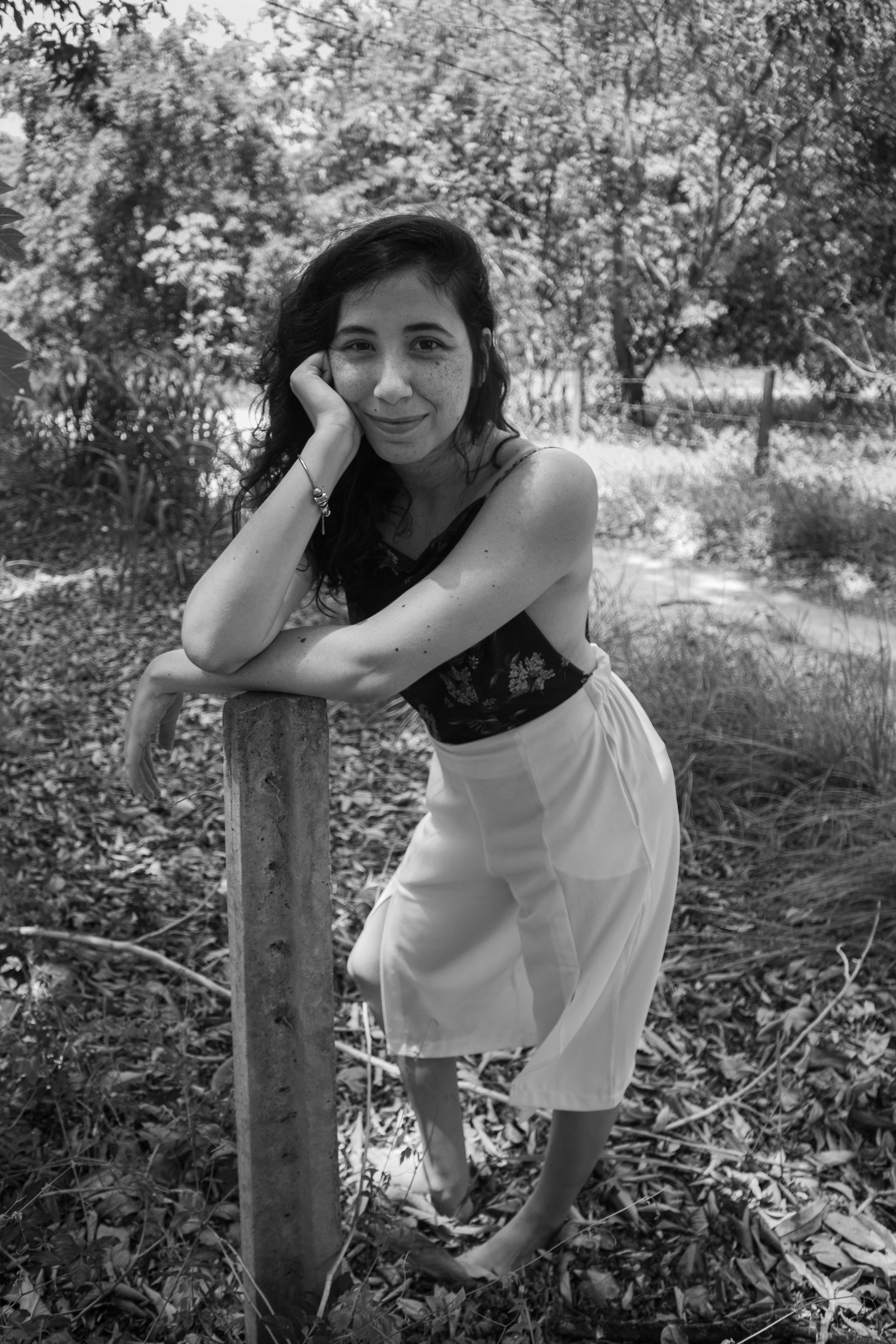 a woman leaning against a wooden post in the woods