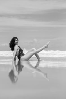 A captivating black and white beach portrait of a woman smiling gracefully while seated in shallow water.