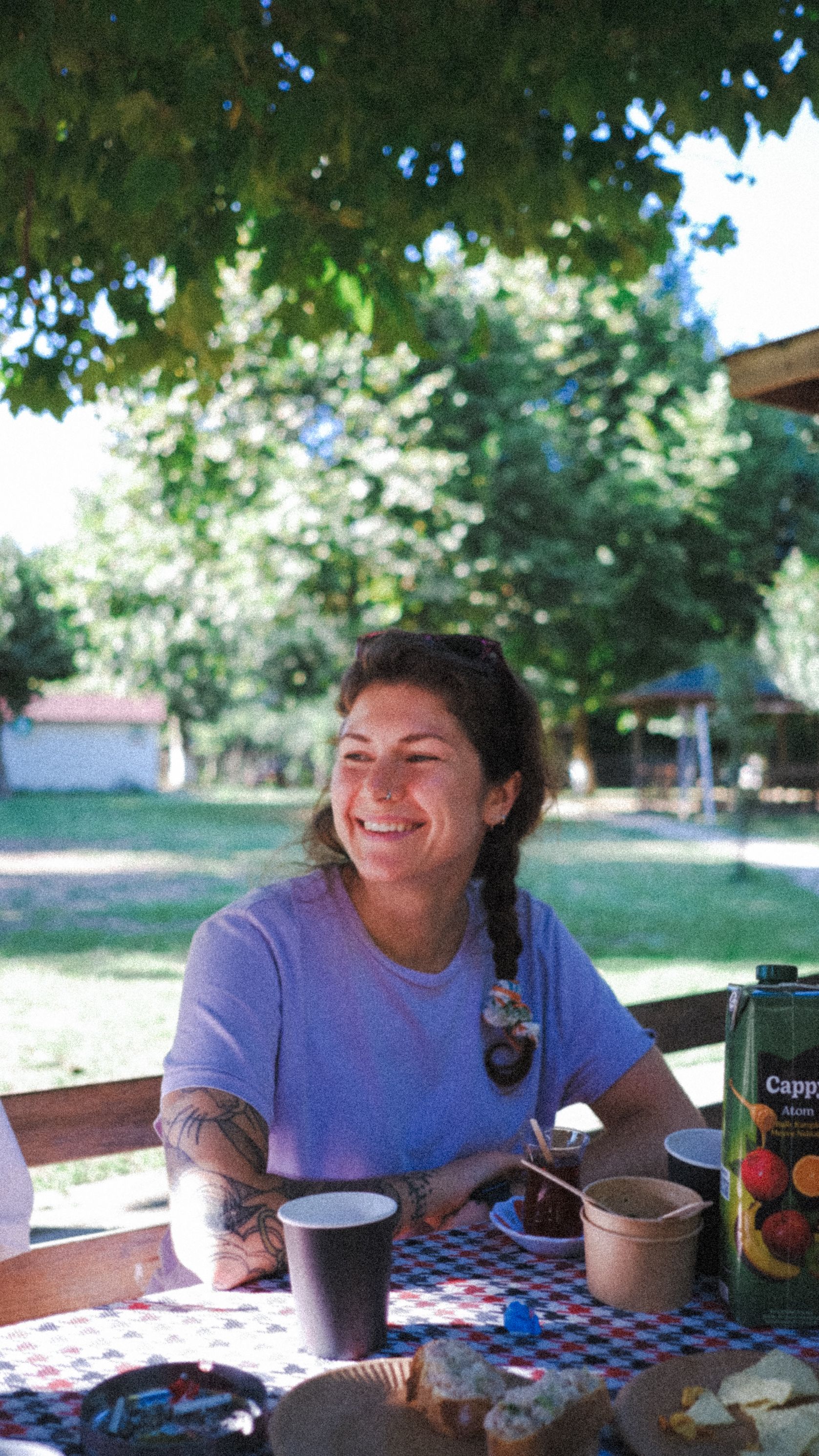 A cheerful woman sitting outdoors at a picnic table, enjoying a sunny day.