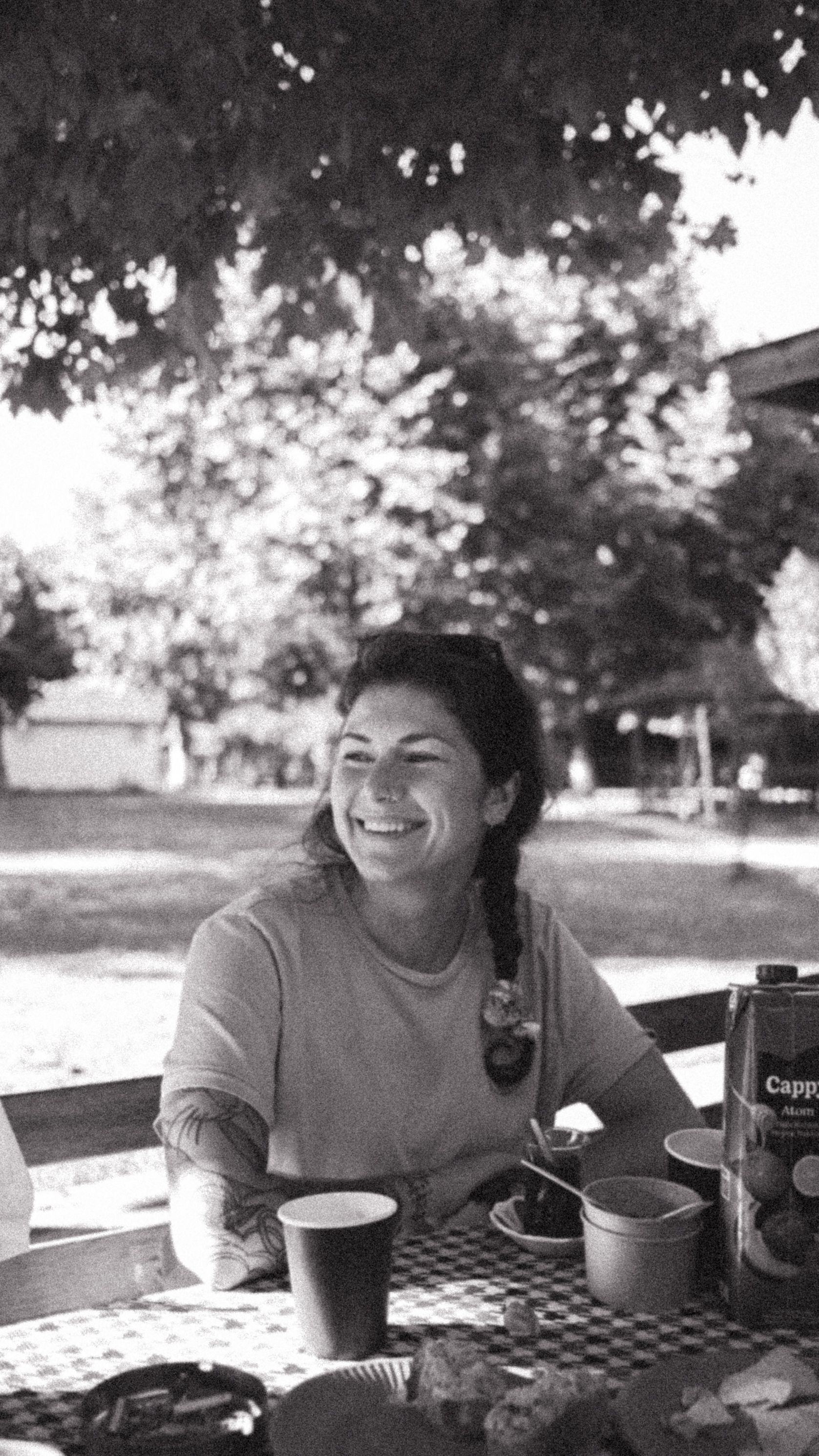 Smiling woman enjoying outdoor picnic under trees, black and white photo.
