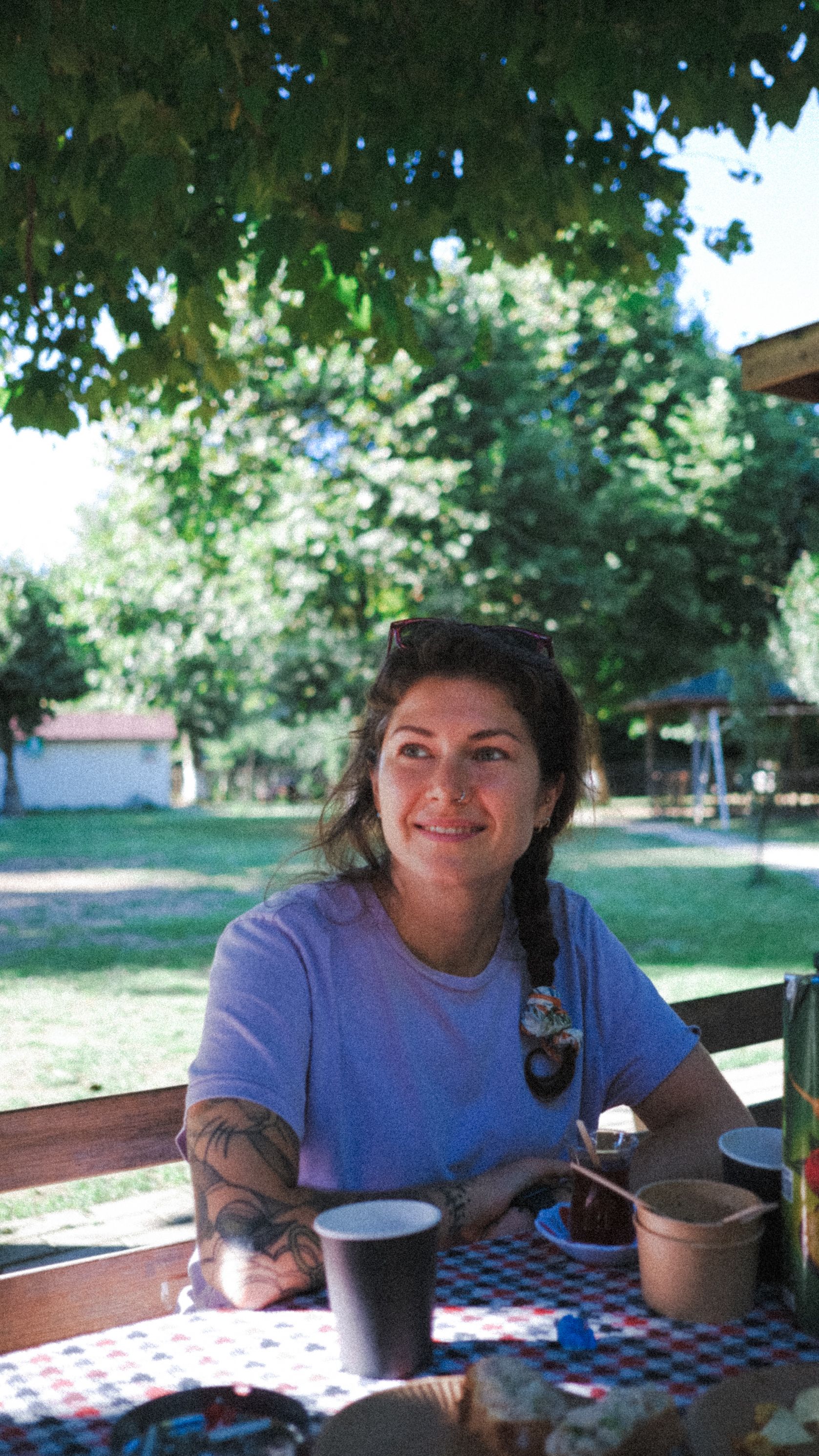 A relaxed woman sits at an outdoor picnic table in a sunny park, enjoying leisure time.