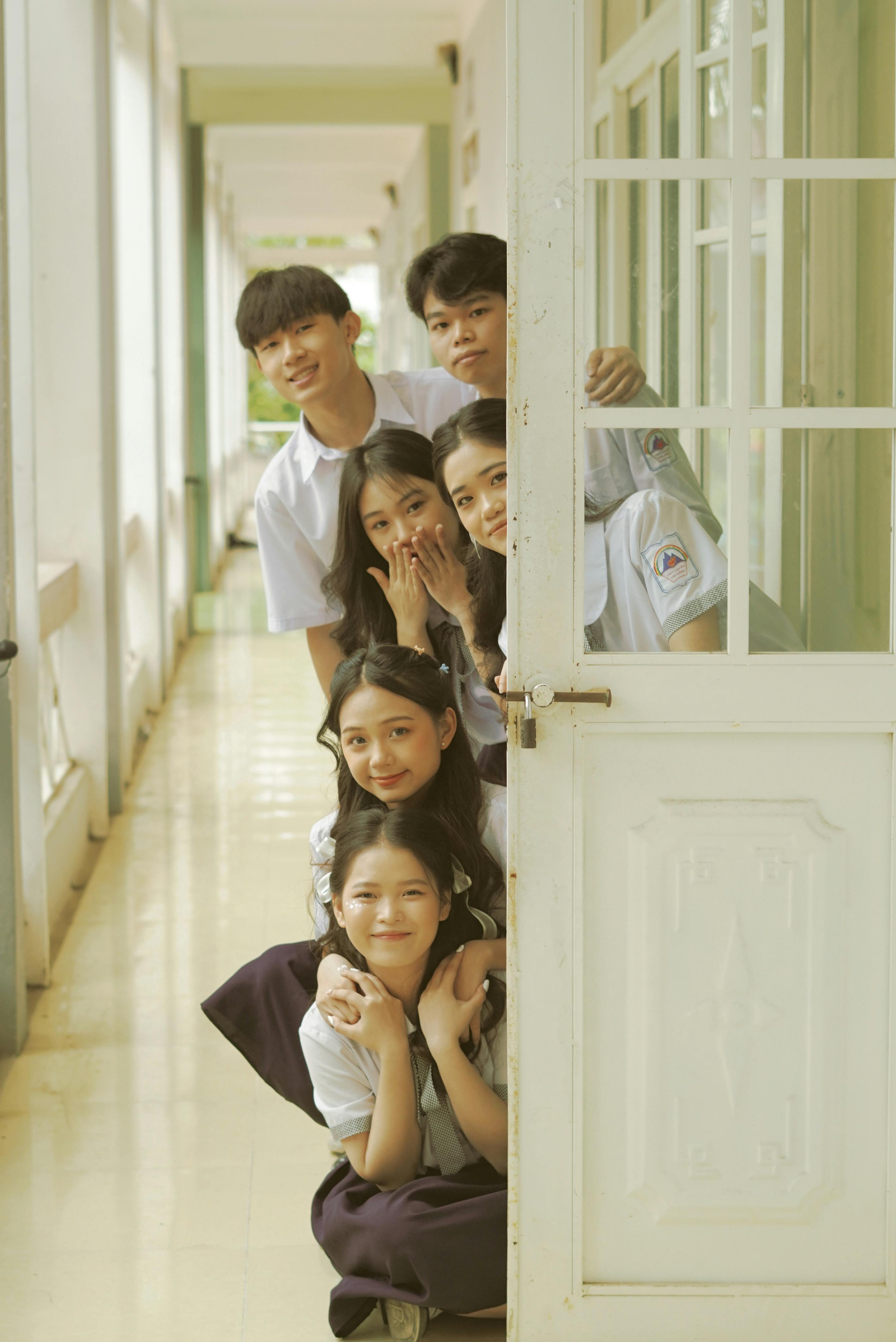 group of students hiding behind a door in a school corridor