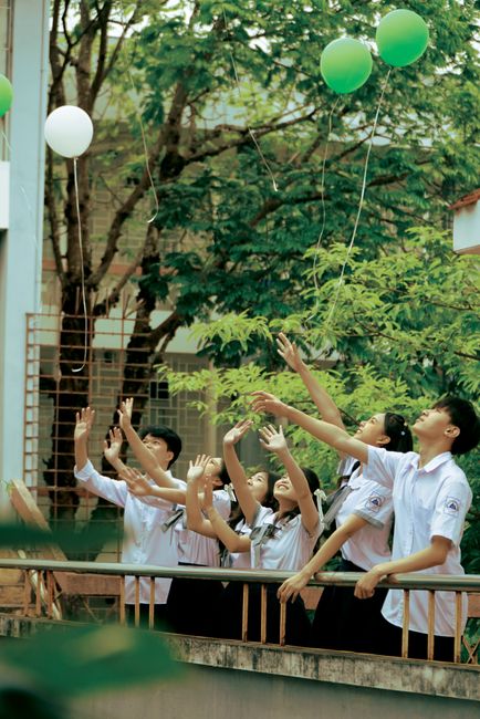 Group of schoolchildren reaching for balloons outdoors, enjoying leisure time.