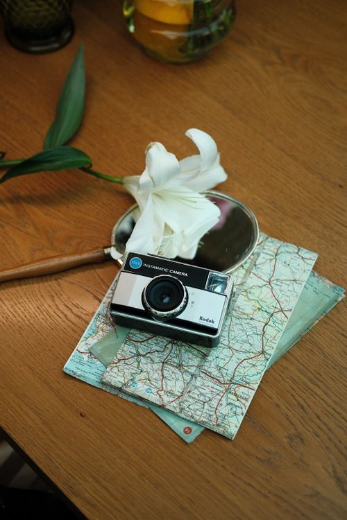Free A retro camera placed on a map with a white lily, evoking travel nostalgia. Stock Photo