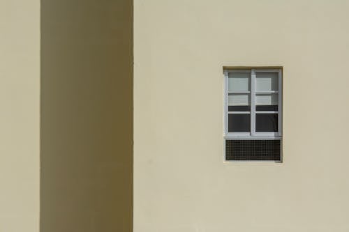 Free Exterior wall showcasing a minimalist design with a single window and air vent. Stock Photo
