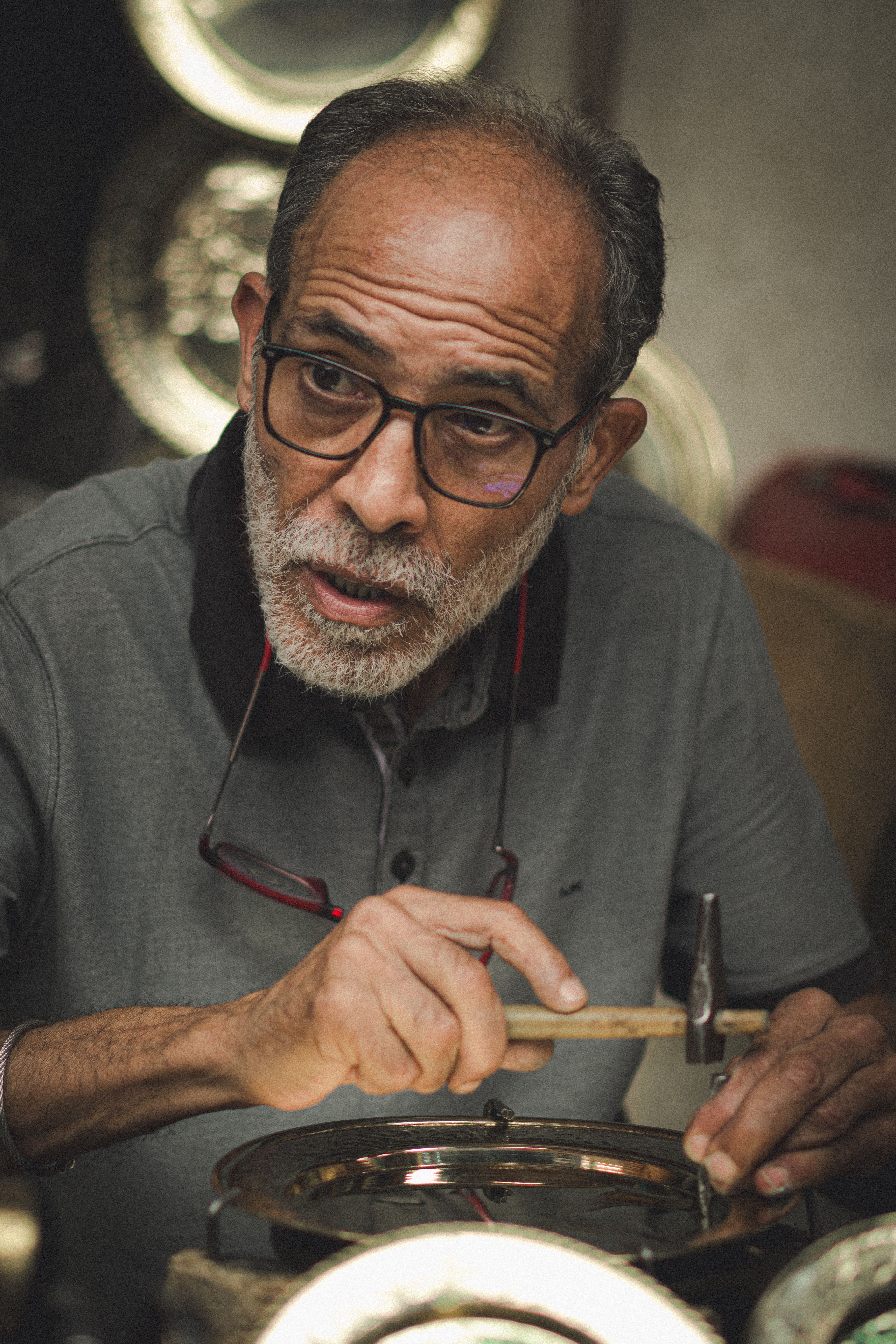 Elderly Tunisian artisan meticulously crafting traditional metalwork in a historic workshop.
