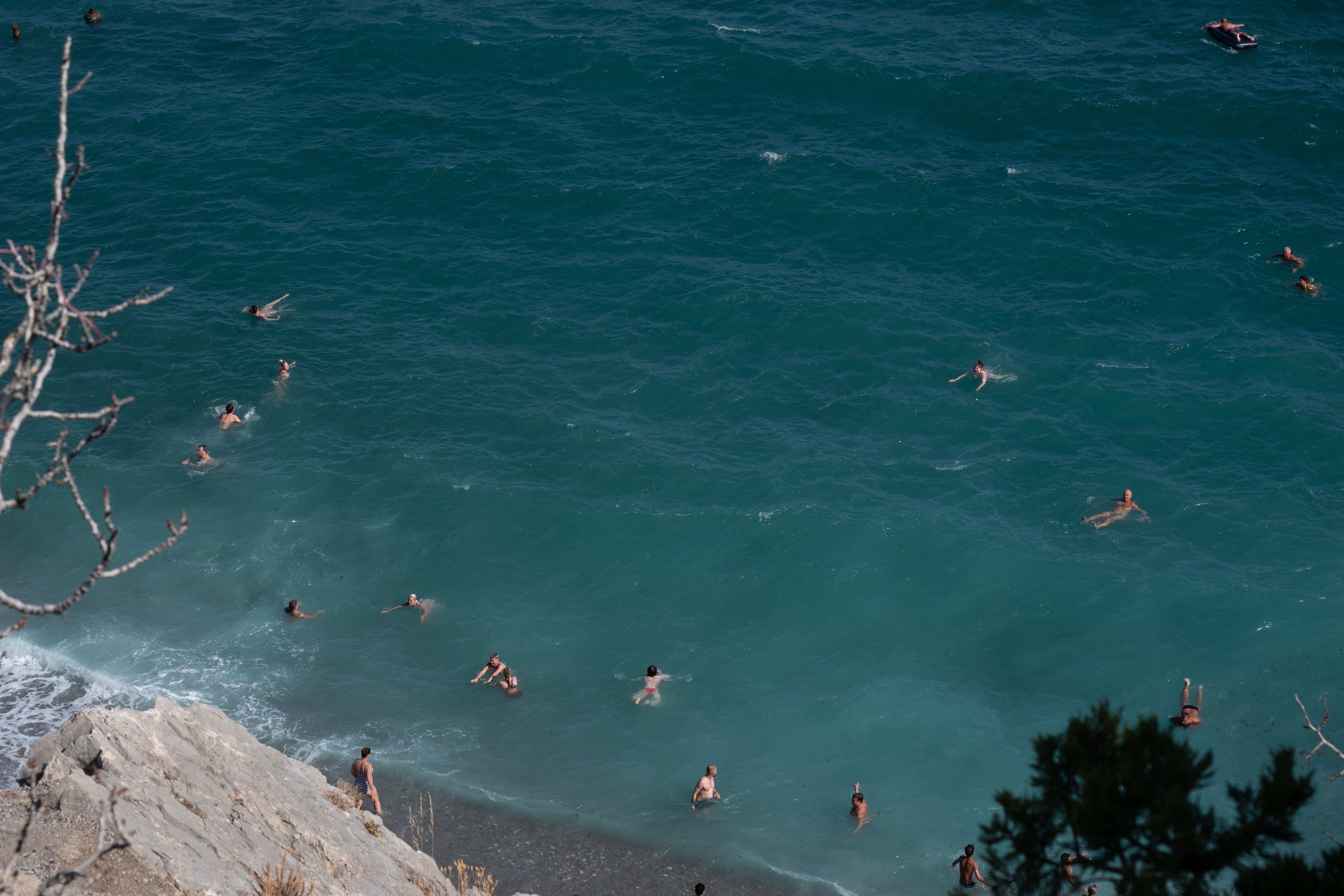 A group of people swimming in the ocean near a rocky cliff · Free Stock ...
