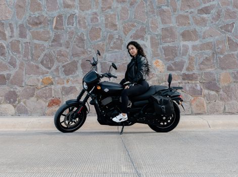 A woman sits confidently on a black motorcycle in San Luis Potosí, outdoor setting.