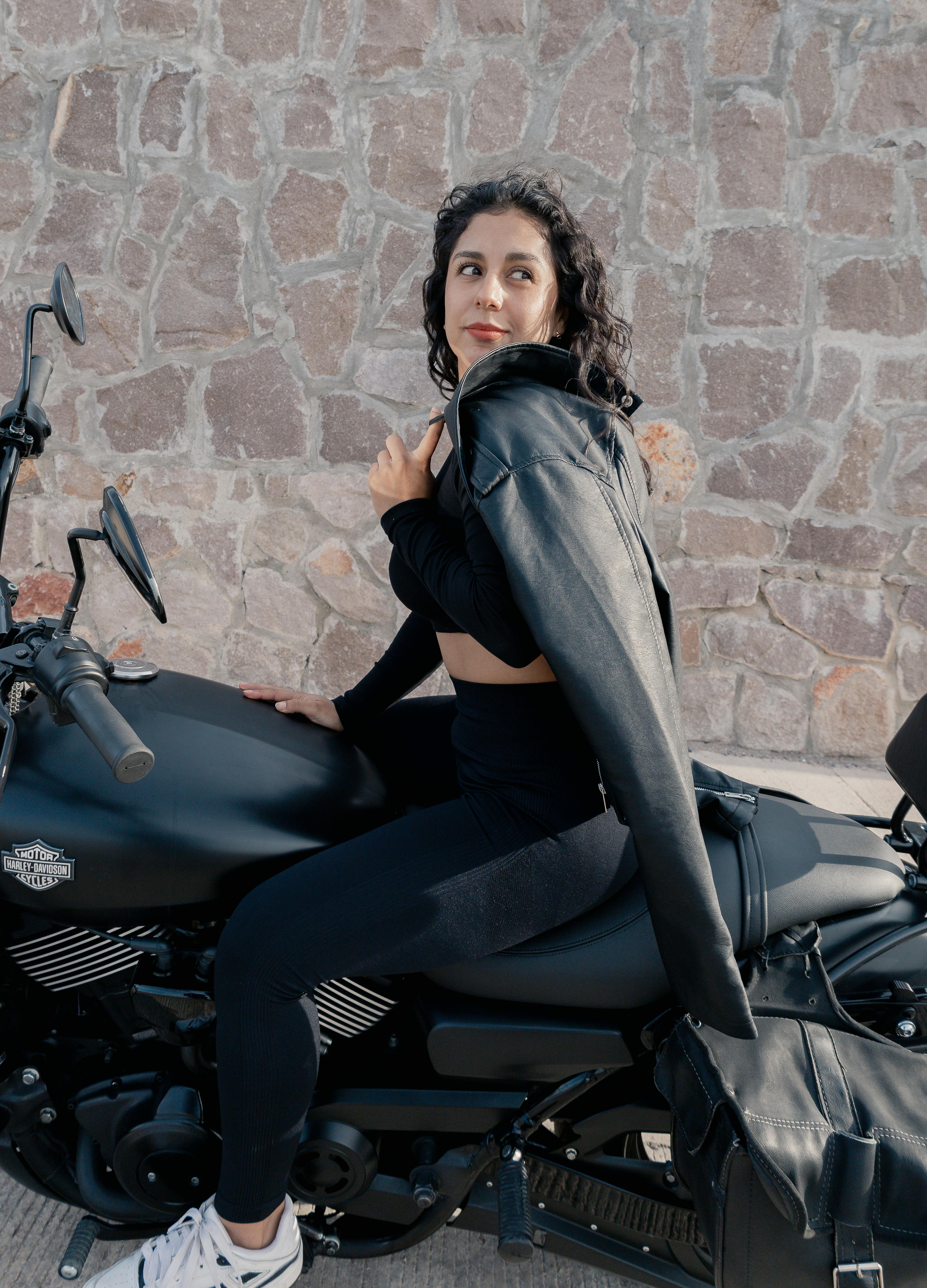 A woman poses confidently on a black motorcycle against a stone wall in San Luis Potosí.