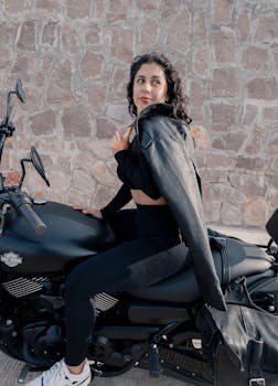 A woman poses confidently on a black motorcycle against a stone wall in San Luis Potosí.