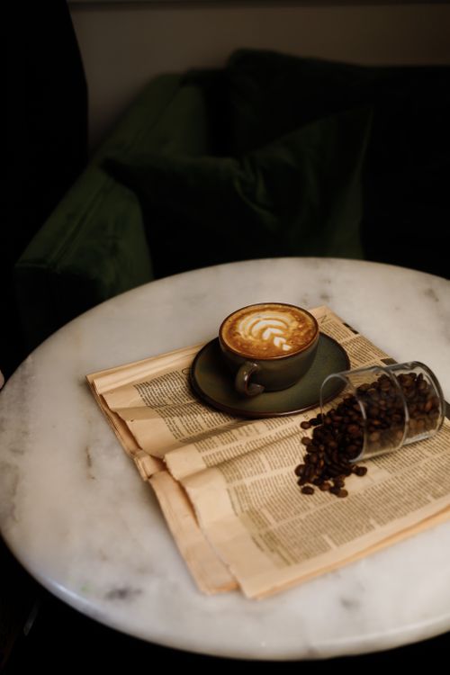 Free A serene morning scene with a cappuccino and coffee beans on a marble table. Stock Photo