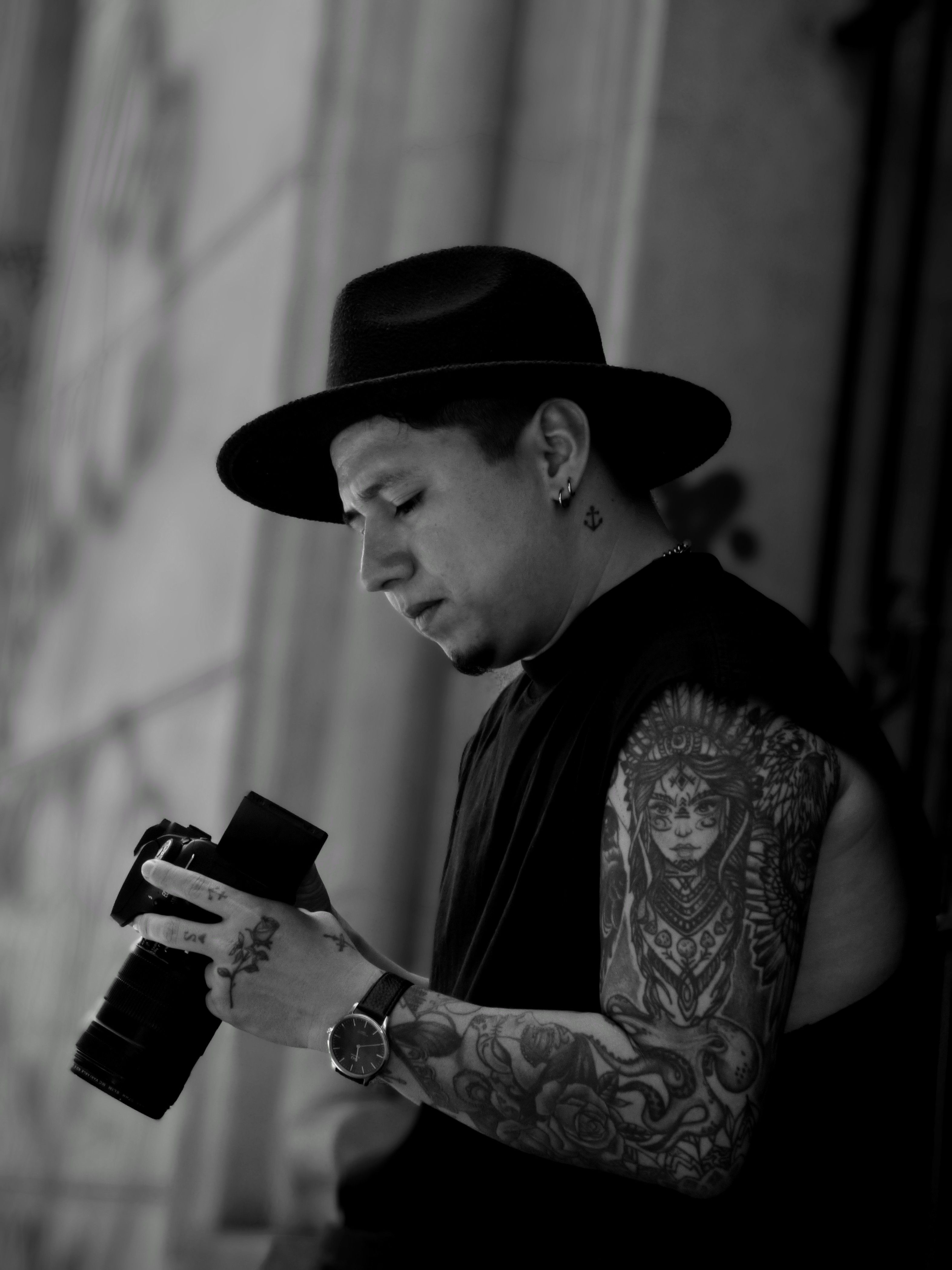 Artistic portrait of a tattooed man holding a camera in a black and white setting.