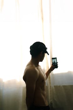 Artistic silhouette of a shirtless man taking a selfie with a phone, showcasing brawny physique.