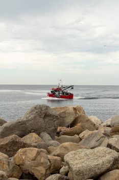 Red fishing boat travels along Porto's rocky coast, capturing a serene seascape scene.