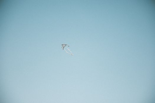 A single kite flying high against a vast clear blue sky, symbolizing freedom and joy.
