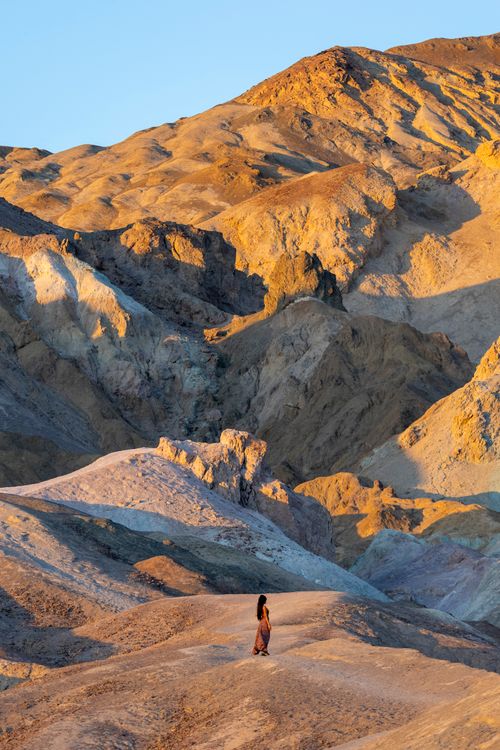 Free A woman stands in a vast eroded desert landscape during sunset. Stock Photo