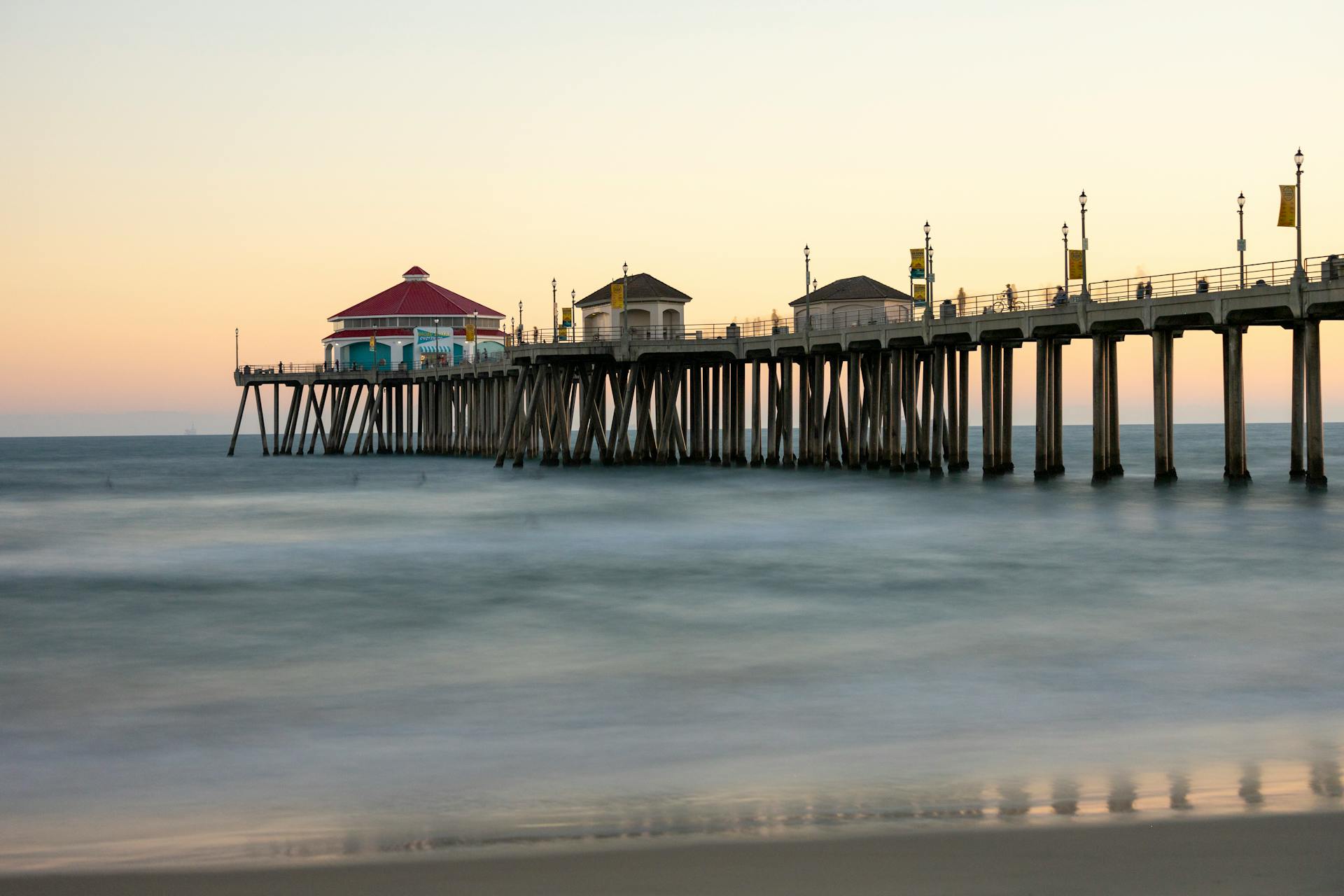 Huntington Beach Pier at sunset with gentle waves and pastel sky tones, ideal for serene coastal imagery.