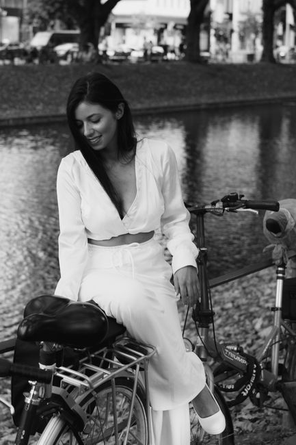 A woman in white relaxes on a bicycle by Düssel Canal, Düsseldorf, exuding elegance.