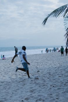 A man playing soccer on the beach, with ocean waves in the background.