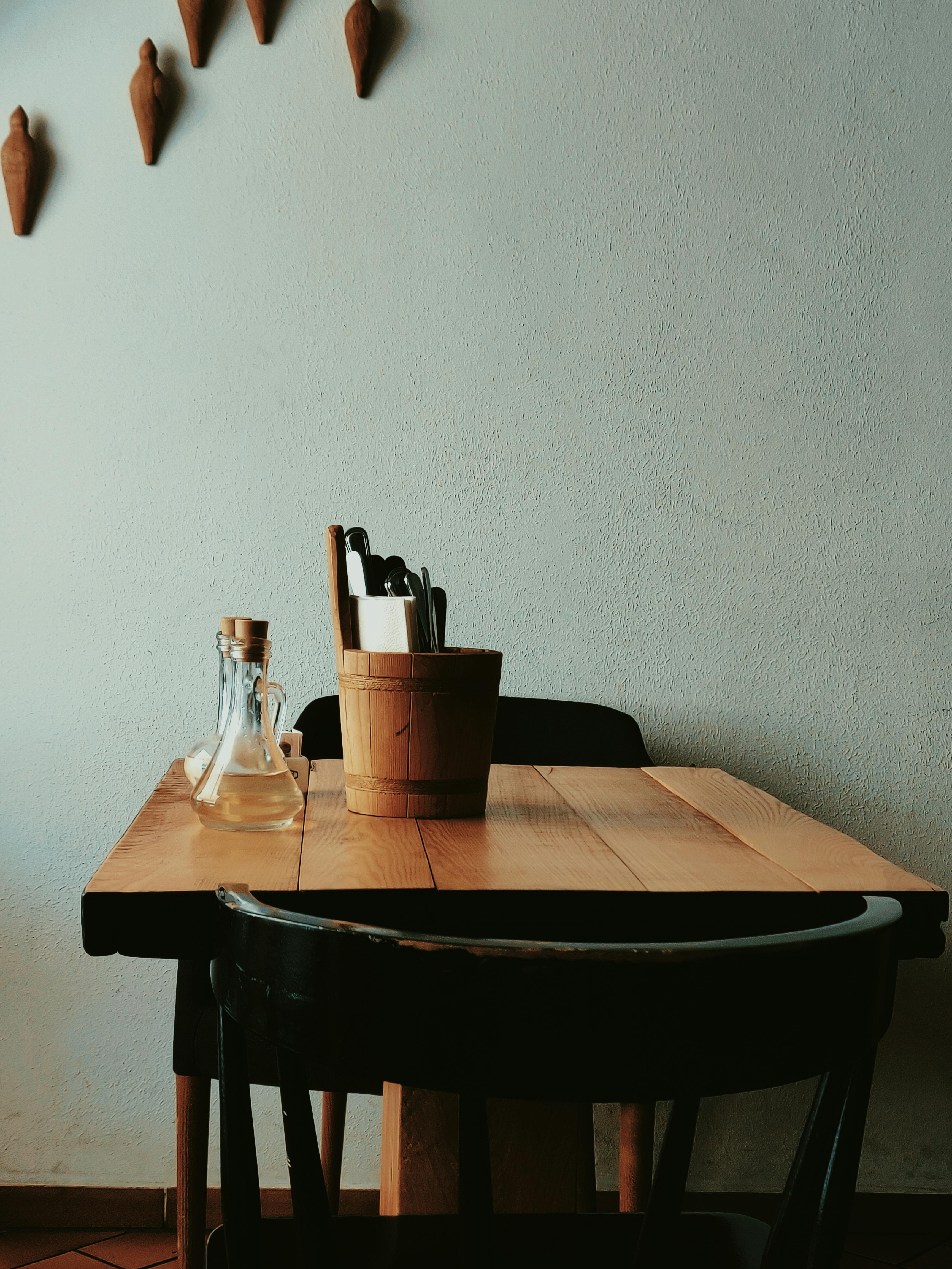 Minimalist wooden dining setup with a bucket of utensils and decorative wall pieces.