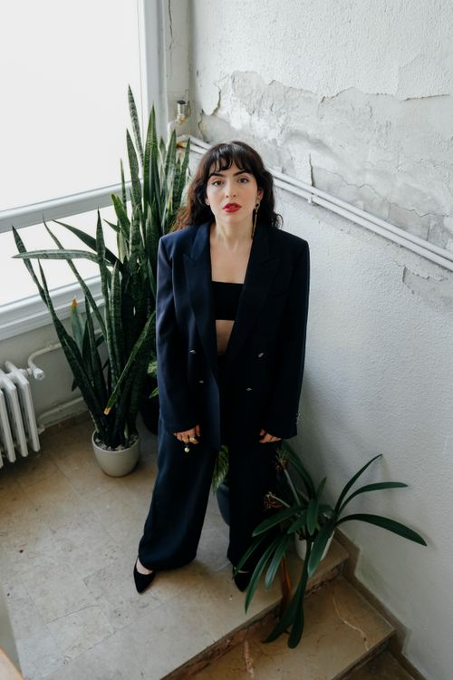 Free Stylish woman in a dark suit poses indoors among plants against a textured wall. Stock Photo