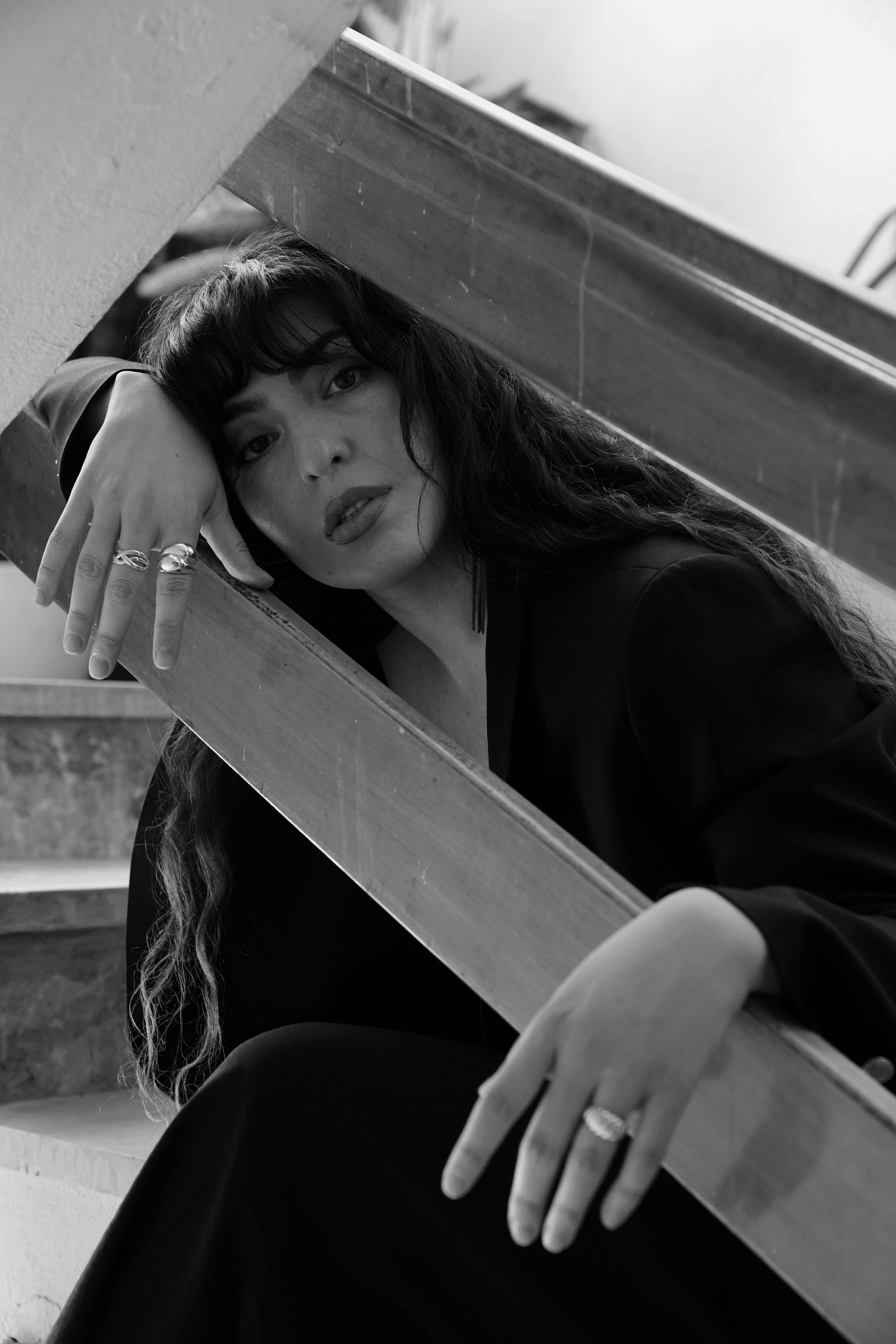 Artistic black and white portrait of a woman in an urban setting, seated on stairs.