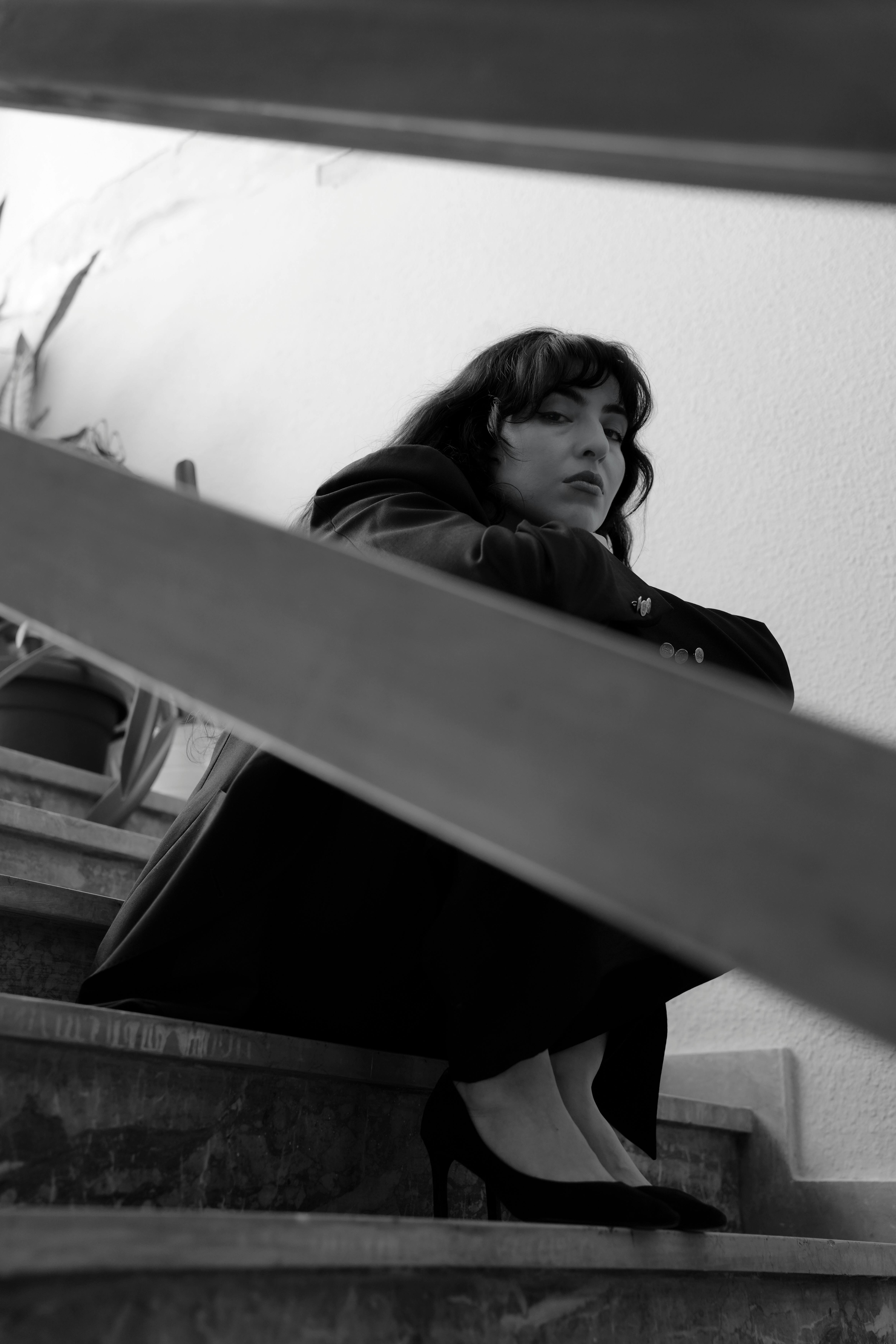 Black and white portrait of a woman seated on stairs, conveying contemplation and mystery.