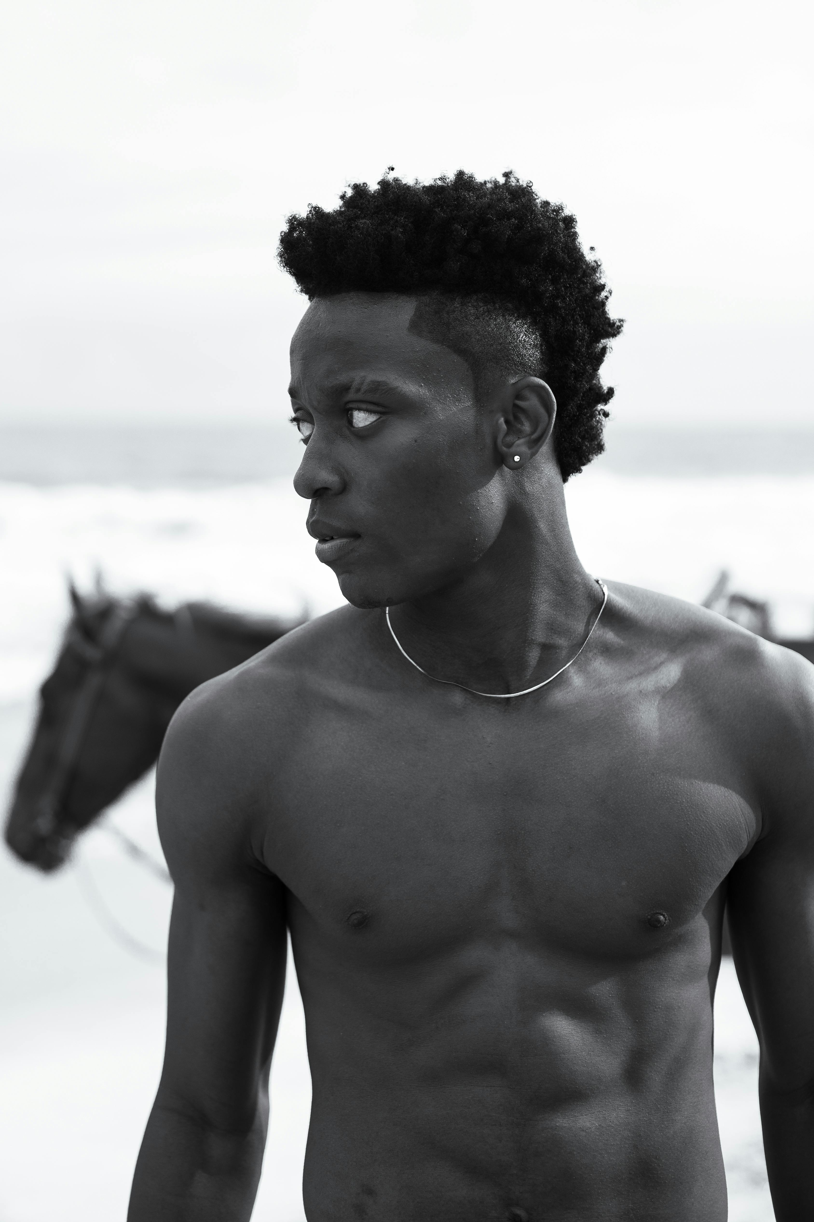 a shirtless man standing on the beach with horses