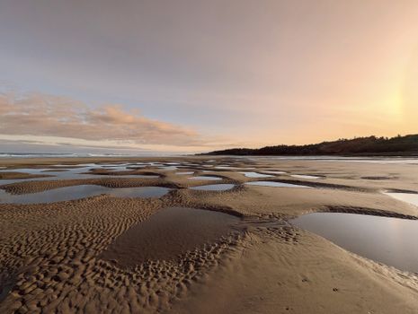 A tranquil beach scene at sunset with unique sand formations and distant waves.