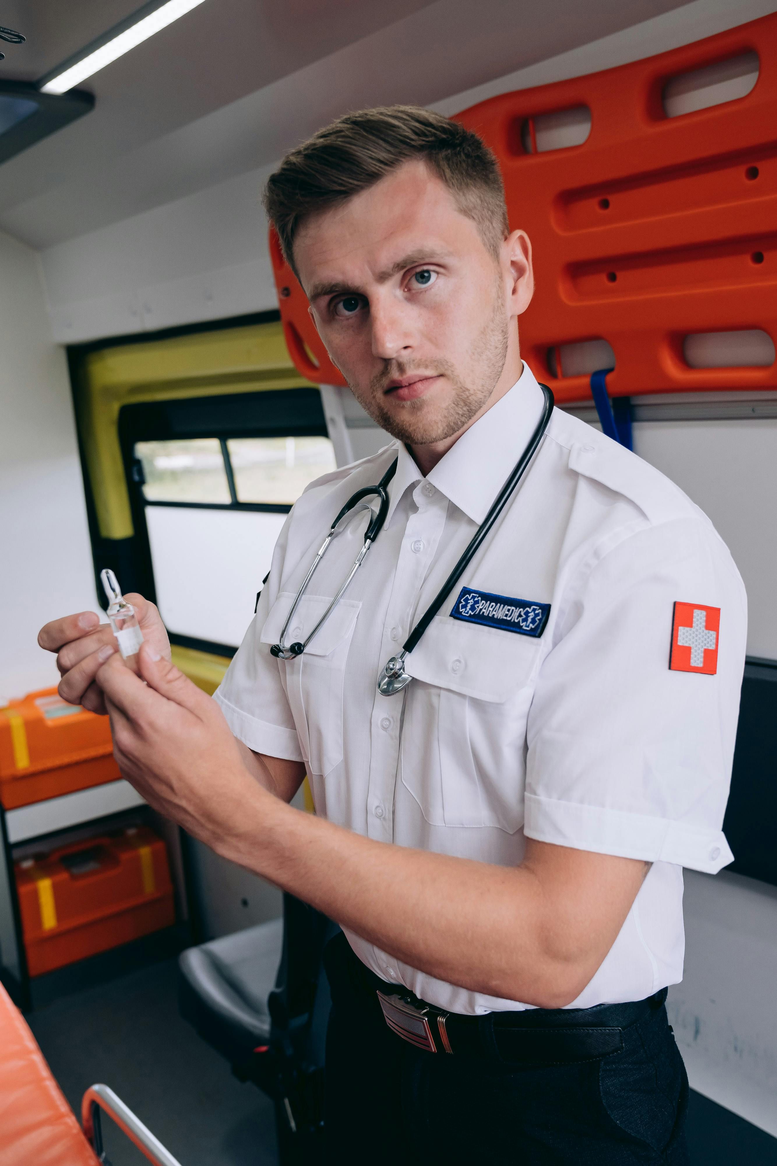 A paramedic stands inside an ambulance holding medical equipment, ready for emergency response.