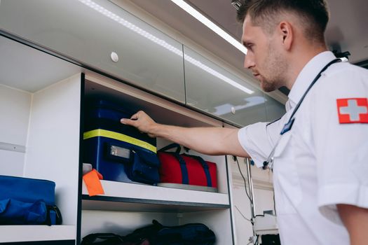 A paramedic organizes medical supplies inside an ambulance shelf for emergency preparedness.