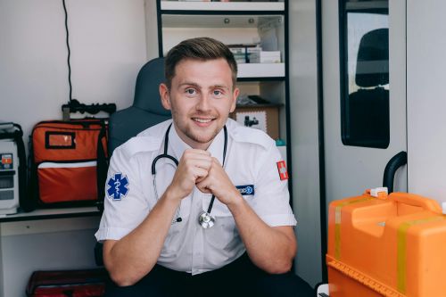 Free Smiling paramedic in uniform with stethoscope inside ambulance. Healthcare and emergency services concept. Stock Photo