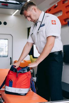 Paramedic in uniform arranges medical bag inside an ambulance, demonstrating readiness and professionalism.